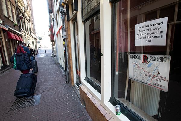 Two tourists pull their suitcases by closed windows of sex workers in the red light district of Amsterdam.