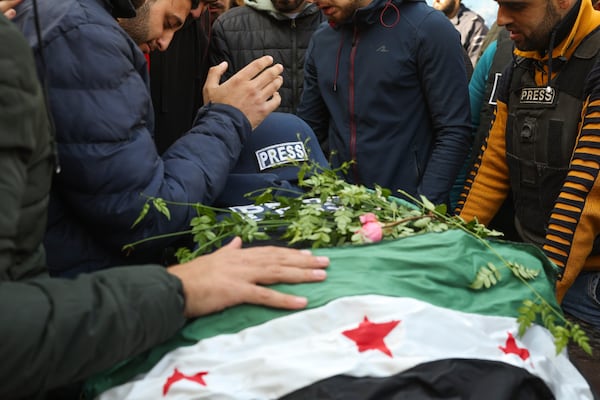 Colleagues and friends mourn over the body, covered with a Syrian opposition flag, of Syrian photographer Anas Alkharboutli, 32, in Idlib, Syria, Wednesday Dec. 4, 2024. Alkharboutli, working for the German news agency DPA was killed in an airstrike near the city of Hama, the agency said Wednesday.(AP Photo/Ghaith Alsayed)