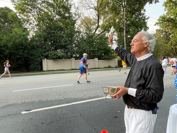 The Rev. Sam Candler of the Cathedral of St. Philip blessed runners with holy water. (Photo: Anjali Huynh/AJC)