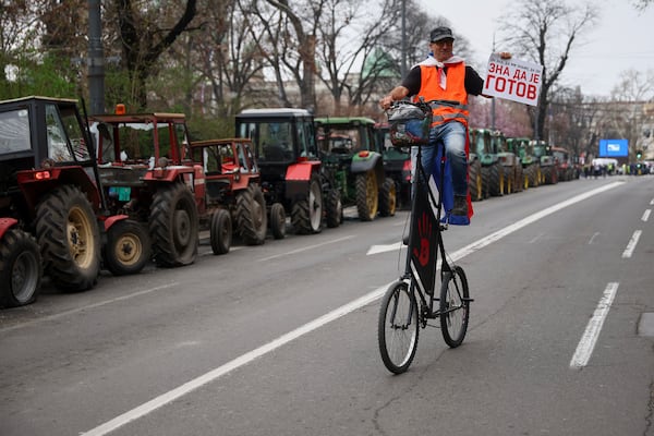 A protester riding past parked tractors carries a placard reading 'he knows he is done' during a major rally against populist President Aleksandar Vucic and his government, in downtown Belgrade, Serbia, Saturday, March 15, 2025. (AP Photo/Armin Durgut)