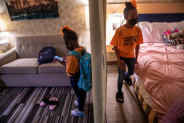 A curtain separates the living room from the bedroom as Runyia McKiver, 10, right, makes the bed she shares with her little sister, Brooklyn Mitchell, left, in their hotel room at Home2 Suites in Newnan. Runyia says she likes being a big sister because she likes to teach her sister Brooklyn new things. (Alyssa Pointer / Alyssa.Pointer@ajc.com)