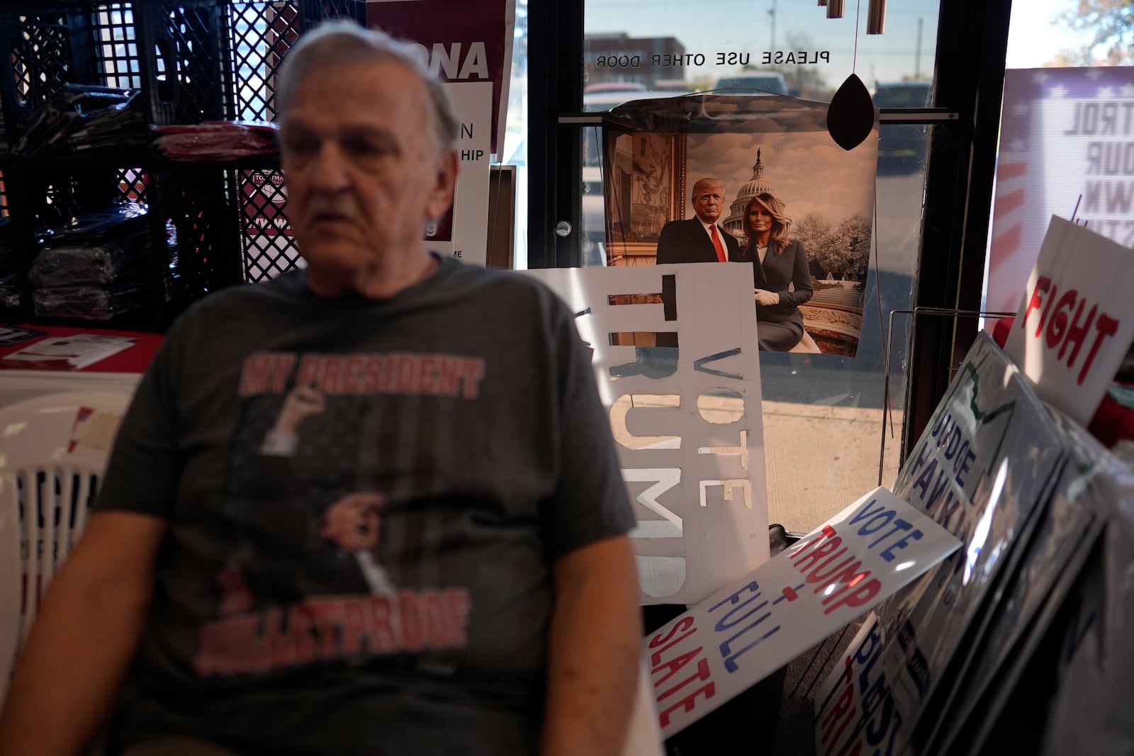 An image of Republican presidential candidate former President Donald Trump and former first lady Melania Trump is seen behind Donald Skowron and his sign and stencil collection after Rep. Jim Jordan, R-Ohio, spoke at a rally for Rep. Michael Rulli, R-Ohio, at the Mahoning County Republican Party headquarters in Boardman, Ohio, Thursday, Oct. 17, 2024. (AP Photo/Carolyn Kaster)