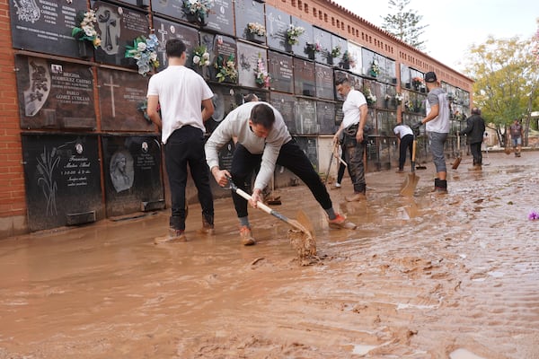 People clear away mud from inside a flood damaged cemetery on the outskirts of Valencia, Spain, Friday, Nov. 1, 2024 after flooding in the region. (AP Photo/Alberto Saiz)