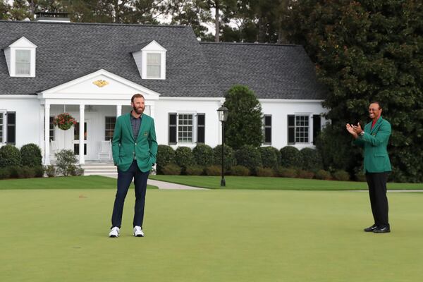 Last year's Masters champion Tiger Woods (right) applauds after presenting Dustin Johnson his first green jacket in front of Butler Cabin for winning the Masters Tournament Sunday, Nov. 15, 2020, at Augusta National. (Curtis Compton / Curtis.Compton@ajc.com)