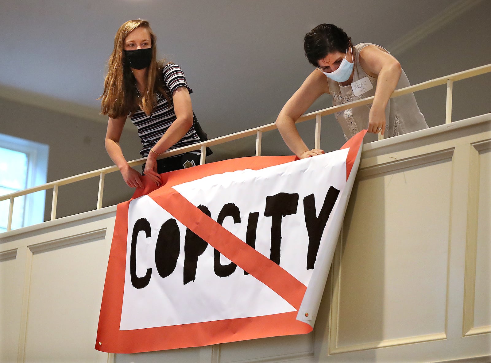 080521 Atlanta: Local activists Kelsea (left) and Nora (right), who go by first names only, hang a "Stop Cop City" banner from the balcony of the Neighborhood Church during a town hall meeting to gather public input in opposition to the plans for a new police and fire training facility in DeKalb County on Thursday, August 5, 2021, in Atlanta.   “Curtis Compton / Curtis.Compton@ajc.com”