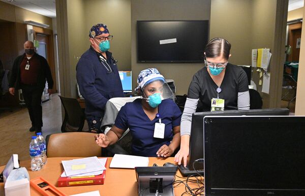 Registered nurses Brandy Harris confers with Kari Ruis, right, at the Intensive Care Unit. "It's super busy," said Harris, who has been a nurse for 21 years. "Wearing this mask all day, it is warm. In and out of the rooms all day. Gloves and gowns, and cleaning each piece of equipment you use with a Covid patient. Lots of procedures. Putting a permanent airway in a patient today because he's been intubated for some time. . .The patients are just as sick with omicron with delta, and the original COVID-19." (Hyosub Shin / Hyosub.Shin@ajc.com).