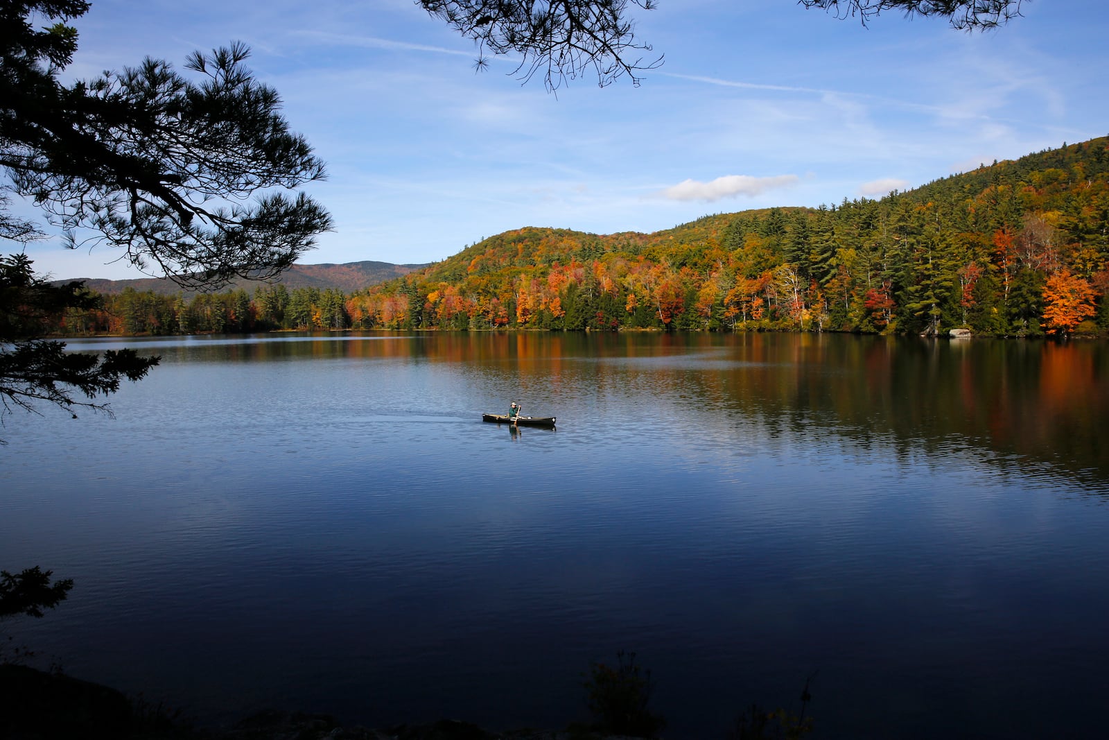 A fly fisherman paddles on a pond as fall foliage begins to show color in Campton, N.H., Sunday, Oct. 6, 2024. (AP Photo/Caleb Jones)