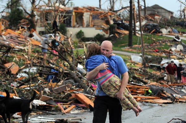 FILE- In this May 22, 2011 file photo, a man carries a young girl who was rescued after a tornado hit Joplin, Mo. (AP Photo/Mike Gullett, File)