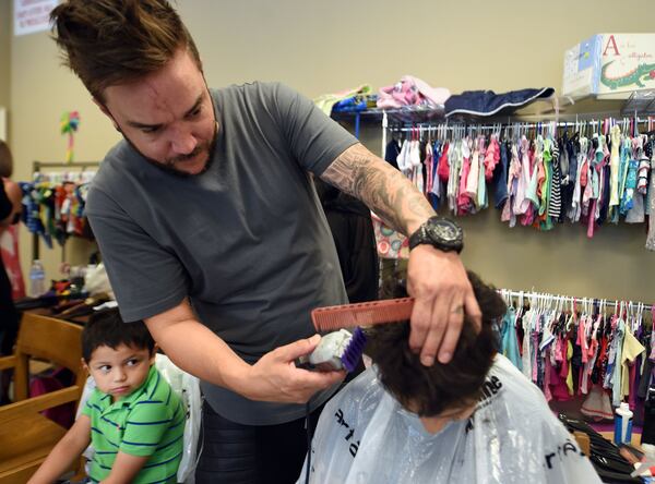 David Chavez (left), 4, waits his turn for a haircut as Matthew Miller works on Joseph Alwadi, 11, on Monday. Miller, of Matthew’s & Co. Salon in Flowery Branch, brought 22 local stylists and assistants to give more than 100 free back-to-school haircuts on Monday. Miller partnered with North Gwinnett Co-op, which helps families in need. KENT D. JOHNSON / KDJOHNSON@AJC.COM