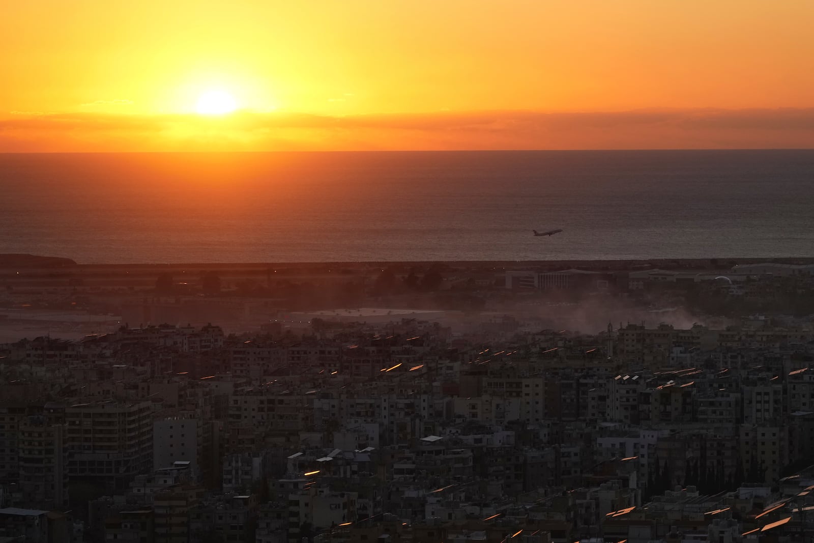 A Middle East Airlines airplane flies over Beirut as smoke rises from Israeli airstrikes in Dahiyeh, Beirut, Tuesday, Oct. 22, 2024. (AP Photo/Hassan Ammar)