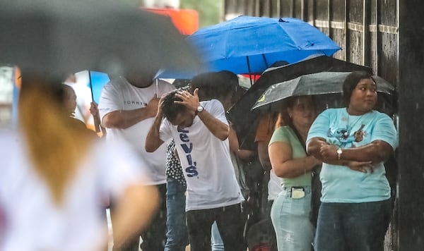 Umbrellas are up on a Tuesday morning in downtown Atlanta in July 2022 as people wait in the rain outside the immigration court at 180 Ted Turner Drive SW. (AJC 2022)