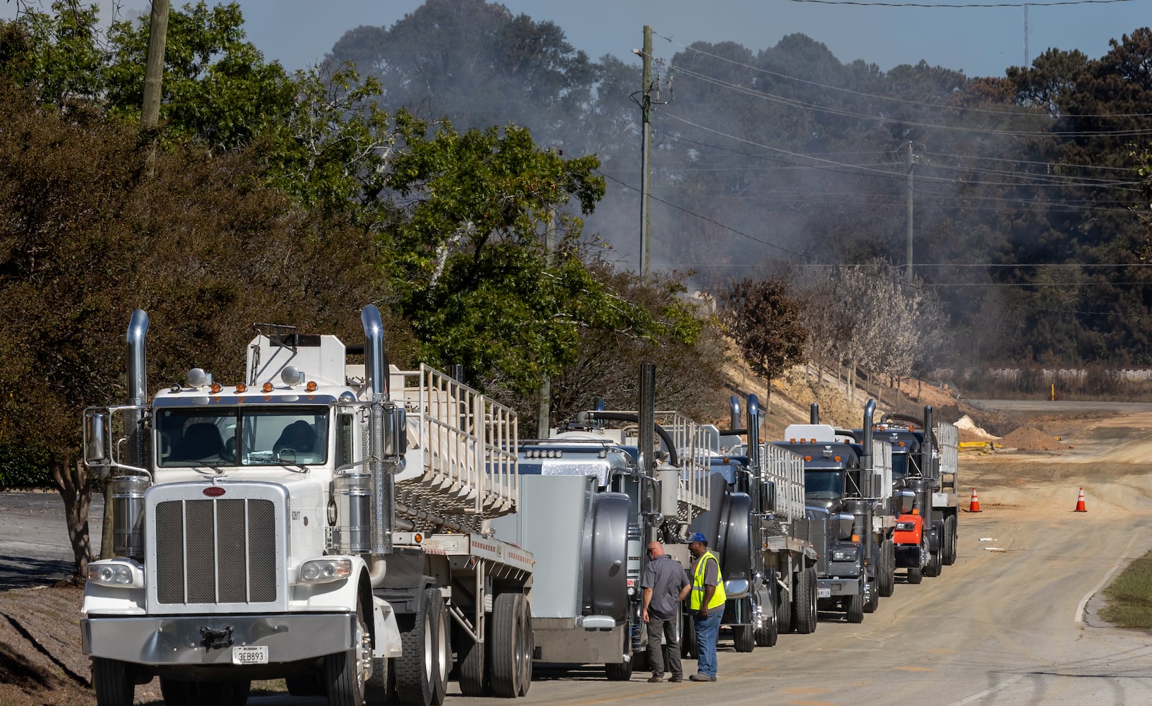 Trucks lined up outside of BioLab along Blackman Road at mid-morning Wednesday, Oct 2, 2024 a large mile-long plume was still visible over Conyers as crews worked at the plant that caught on fire days earlier. But as the sun lifted above the horizon, so did the shelter-in-place order for Rockdale County residents. Those living nearby have been advised to stay inside every evening through early morning until Friday. (John Spink/AJC)