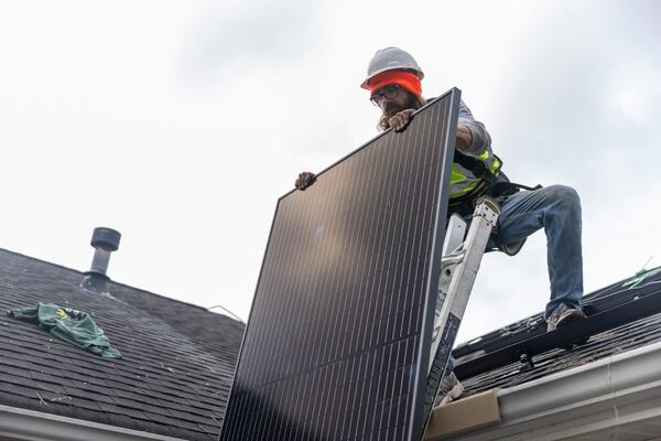 Joe McClain, an installer for Creative Solar USA, moves solar panels onto the roof of a home in Ball Ground, Georgia, on December 17th, 2021. (Nathan Posner for The Atlanta Journal-Constitution)