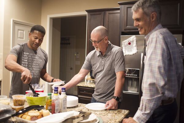 Lee Jenkins, Stephen Gilkenson and Matthew Hendley, left to right, grab food before sitting down at Eddie L. Johnson’s house in Alpharetta on Monday night. (Jenna Eason / Jenna.Eason@coxinc.com)