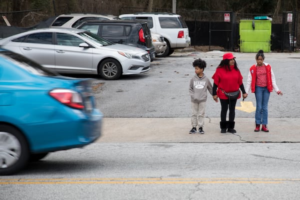 District 12 resident Joyce Smith hold the hands of her grandchildren as they cross the street on Browns Mill Road in south Atlanta. (Riley Bunch/AJC)