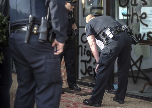 Police officers inspect a note found on the door of the Democratic Party office in Norman, Oklahoma, on Wednesday, April 3, 2019, where vandals spray-painted racist, anti-gay and anti-Semitic graffiti on the entrance to the office. The building, a school and an art center were hit with graffiti the night before. Allison Christine Johnson, 45, of Norman,  is accused of vandalizing buildings in Oklahoma City and Norman over the span of several weeks. Johnson turned herself in to police Thursday, April 4.