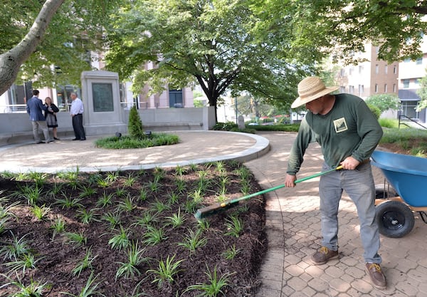 Landscaper Jose Vega (foreground) readies Pershing Point Park for a ceremony rededicating a monument erected to the memory of Fulton County residents killed in World War I. HYOSUB SHIN / HSHIN@AJC.COM