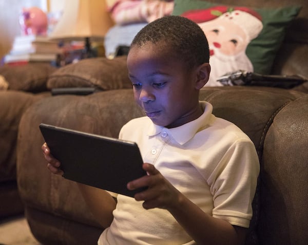 Kristopher Moses, 8, plays a game on his tablet at his family’s residence in Decatur. He was adopted by twin sisters Patricia and Priscilla, who fostered him. They said he is very interested in computers and technology. 