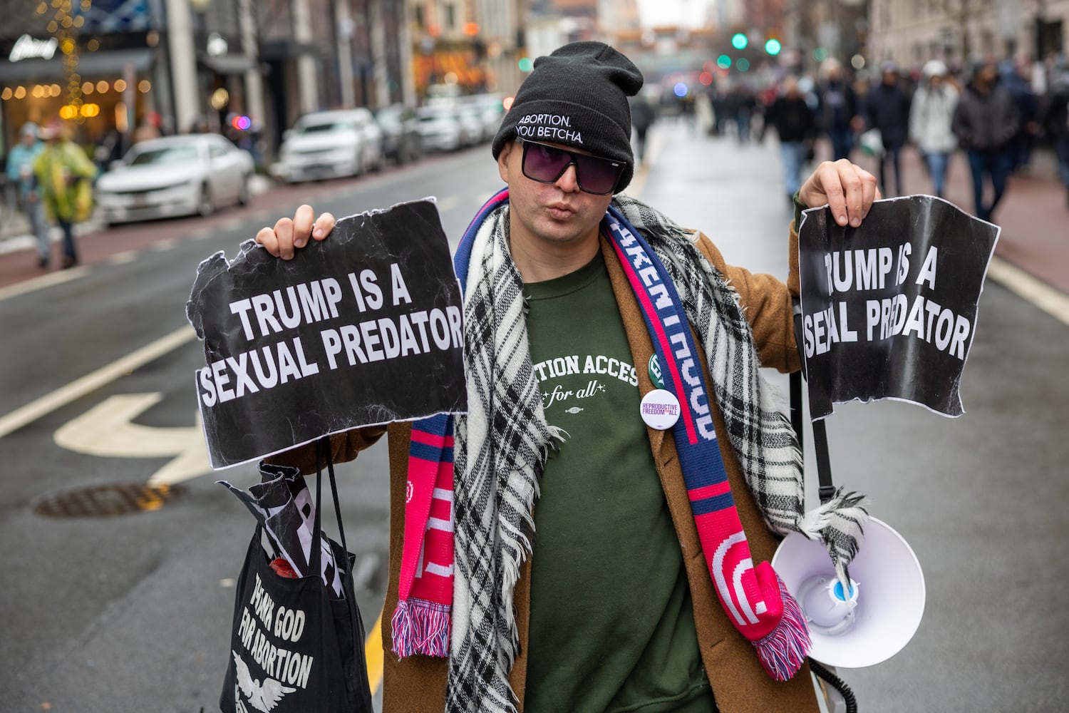 An anti-Trump protestor protests near people waiting to enter a Trump rally at Capital One Arena in Washington, D.C. on Sunday, January 19, 2025, one day before Donald Trump’s inauguration. (Arvin Temkar / AJC)