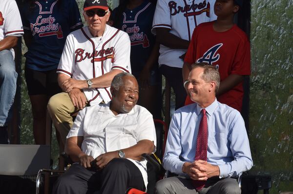 Baseball great Hank Aaron  and Braves CEO  Derek Schiller share a smile at ceremony announcing 2021 All-Star game.  Former Braves star Phil Niekro is seated behind them.