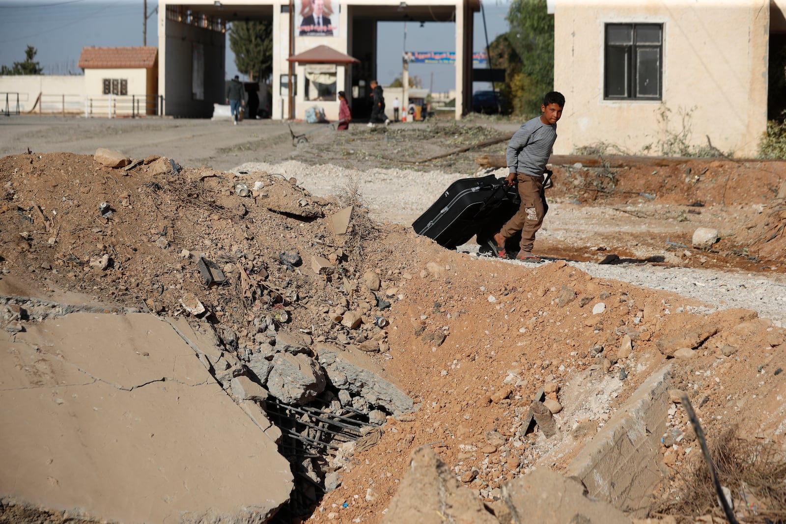 A Syrian boy fleeing the war in Lebanon carries his luggages as he passes through a crater caused by an Israeli airstrike, which blocks the road between the Lebanese and the Syrian crossing points, in Jousieh, Syria, Sunday, Oct. 27, 2024. (AP Photo/Omar Sanadiki)