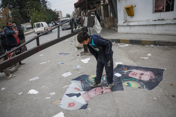 A boy steps over pictures of Syrian President Bashar Assad and his late father, Hafez Assad, right, Salamiyah, east of Hama, Syria, Saturday Dec. 7, 2024. (AP Photo/Ghaith Alsayed)