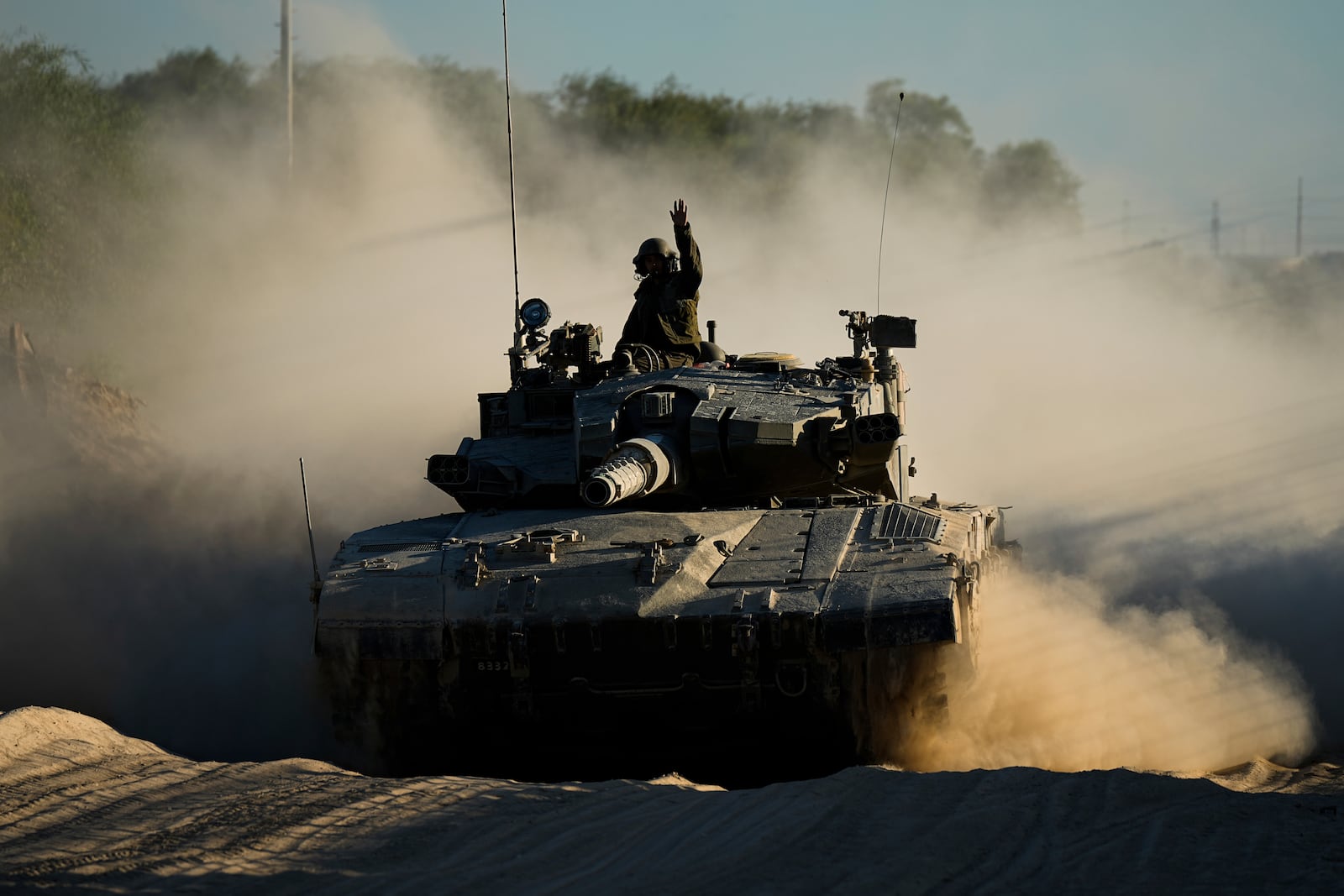 An Israeli soldier waves from a moving tank near the Israeli-Gaza border in southern Israel, Monday, Oct. 21, 2024. (AP Photo/Tsafrir Abayov)