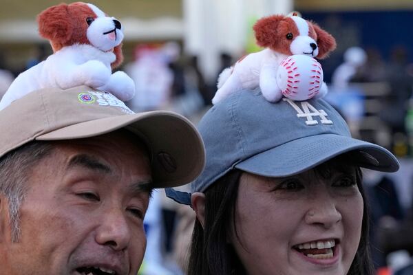 A couple wears cap featuring the pet dog of Los Angeles Dodgers' Shohei Ohtani, before an MLB Japan Series baseball game between the Los Angeles Dodgers and the Chicago Cubs at Tokyo Dome, in Tokyo, Tuesday, March 18, 2025. (AP Photo/Shuji Kajiyama)