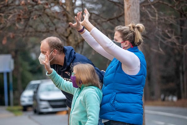 E. Rivers Elementary School third grader Leah French joins her parents, Brooke and Jonathan French, as they wave through a window at her sister, Claire, as she makes her way down the hallway on Jan. 25 during the first day of in-person learning. (Alyssa Pointer / Alyssa.Pointer@ajc.com)