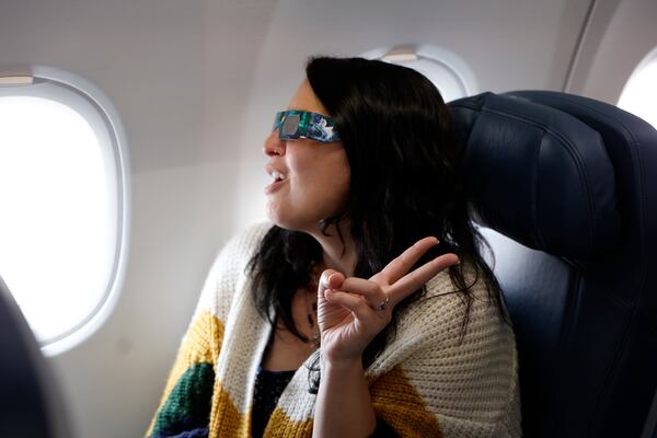 Melanie Elliott from Chapel Hill, NC poses for a photo in here solar eclipse glasses on the flight from Dallas Fort Worth International Airport to Detroit Metro Airport on Monday, April 8, 2024. (Natrice Miller/ AJC)