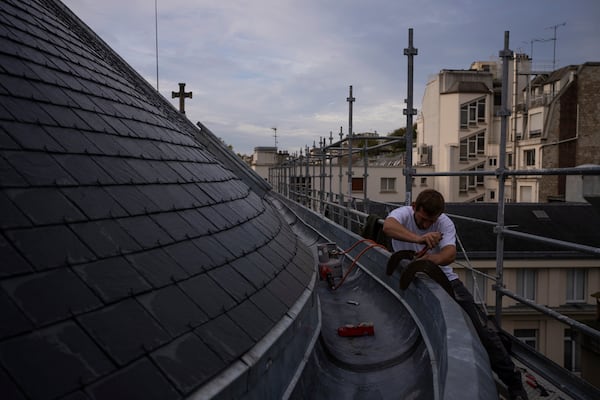 A roofer solders on the zinc gutter of a church in Paris, Tuesday, Oct. 15, 2024. (AP Photo/Louise Delmotte)