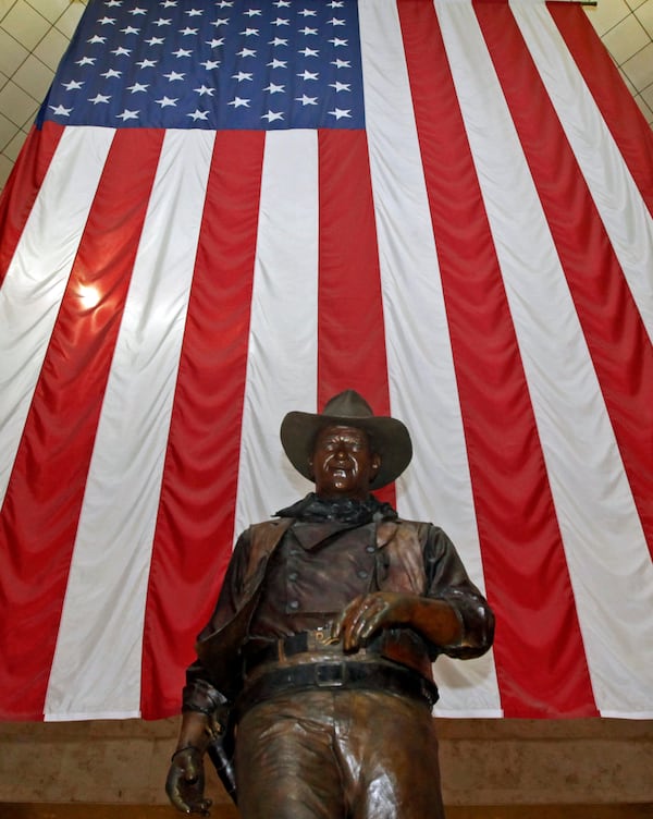 A bronze statue of late actor John Wayne stands before a four-story high U.S. flag at John Wayne Orange County Airport in Santa Ana, California. Officials want the statue removed.