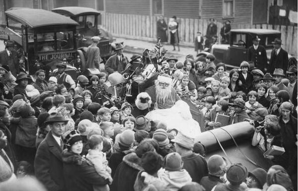 Children, parents and other folks celebrating the season surround Santa Claus as he rides through a Christmas parade in Atlanta, 1920.