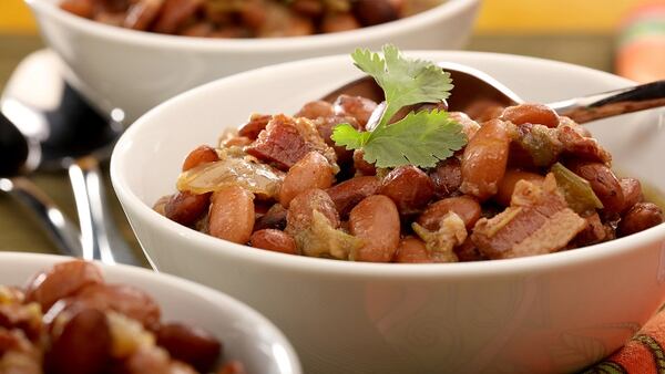 Pinto beans are cooked with bacon, then served with grated cheese and fresh cilantro.  (Michael Tercha/Chicago Tribune/TNS)