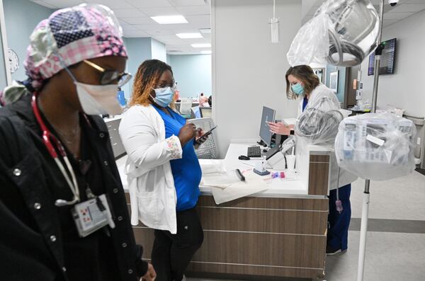 Kamika Shivers, center, and Katie Van Hook, right, both registered ICU nurses, check messages while working a COVID floor at Memorial Health's Heart and Vascular Institute in Savannah. Shivers, who compares COVID-19 waves to hurricane seasons, says of the current wave, “This one is just vicious.” (Hyosub Shin / Hyosub.Shin@ajc.com)