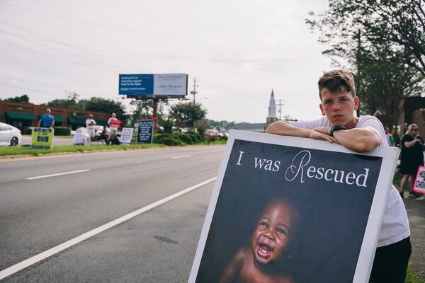 Judah Metzger, 14, stands with a poster outside of an abortion clinic in Forest Park in July. (Olivia Bowdoin for The Atlanta Journal-Constitution)