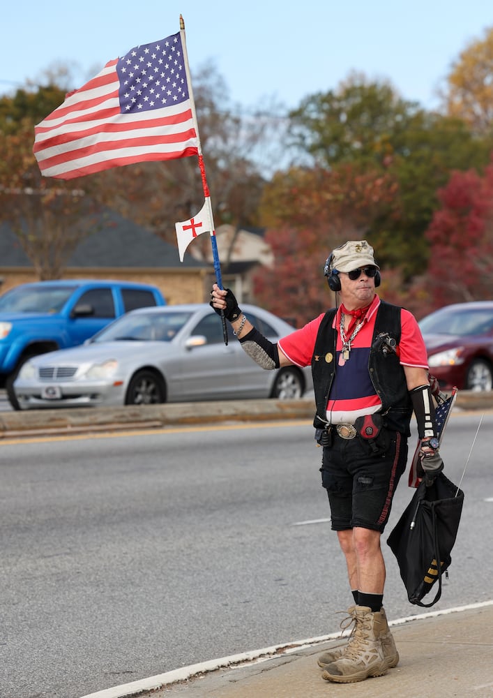 Mark A. Jones waves an American flag to drivers at the intersection one Jimmy Carter Blvd & Buford Highway. PHIL SKINNER FOR THE ATLANTA JOURNAL-CONSTITUTION