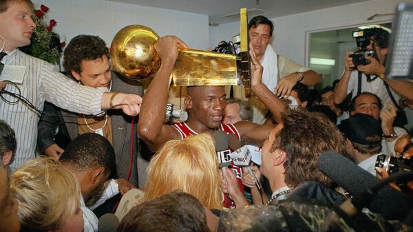 Chicago Bulls Michael Jordan holds the NBA Championship trophy aloft while talking with the media in the locker room after clinching the title with an 108-101 win against the Los Angeles Lakers Wednesday, June 13, 1991, at Inglewood, Calif. (Reed Saxon/AP)