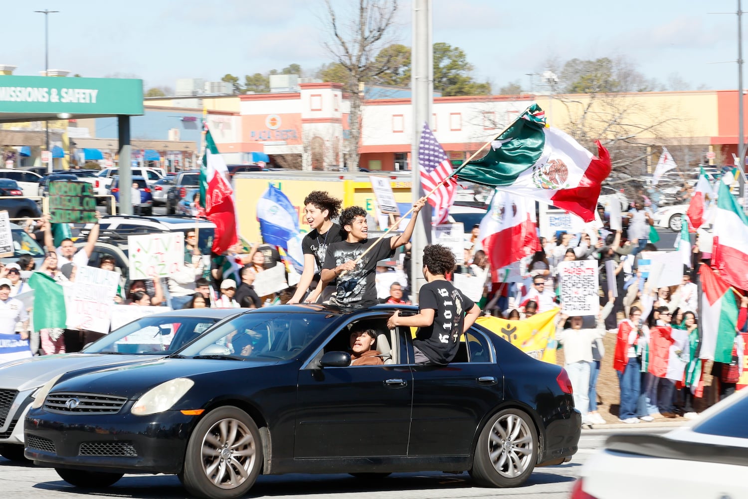 People wave Mexican flags as they ride along Buford Highway. At the same time, protesters chant on the sidewalks of Plaza Fiesta on Saturday, Feb 1, 2025, to demonstrate in response to a recent immigration arrest in Georgia. 
(Miguel Martinez/ AJC)