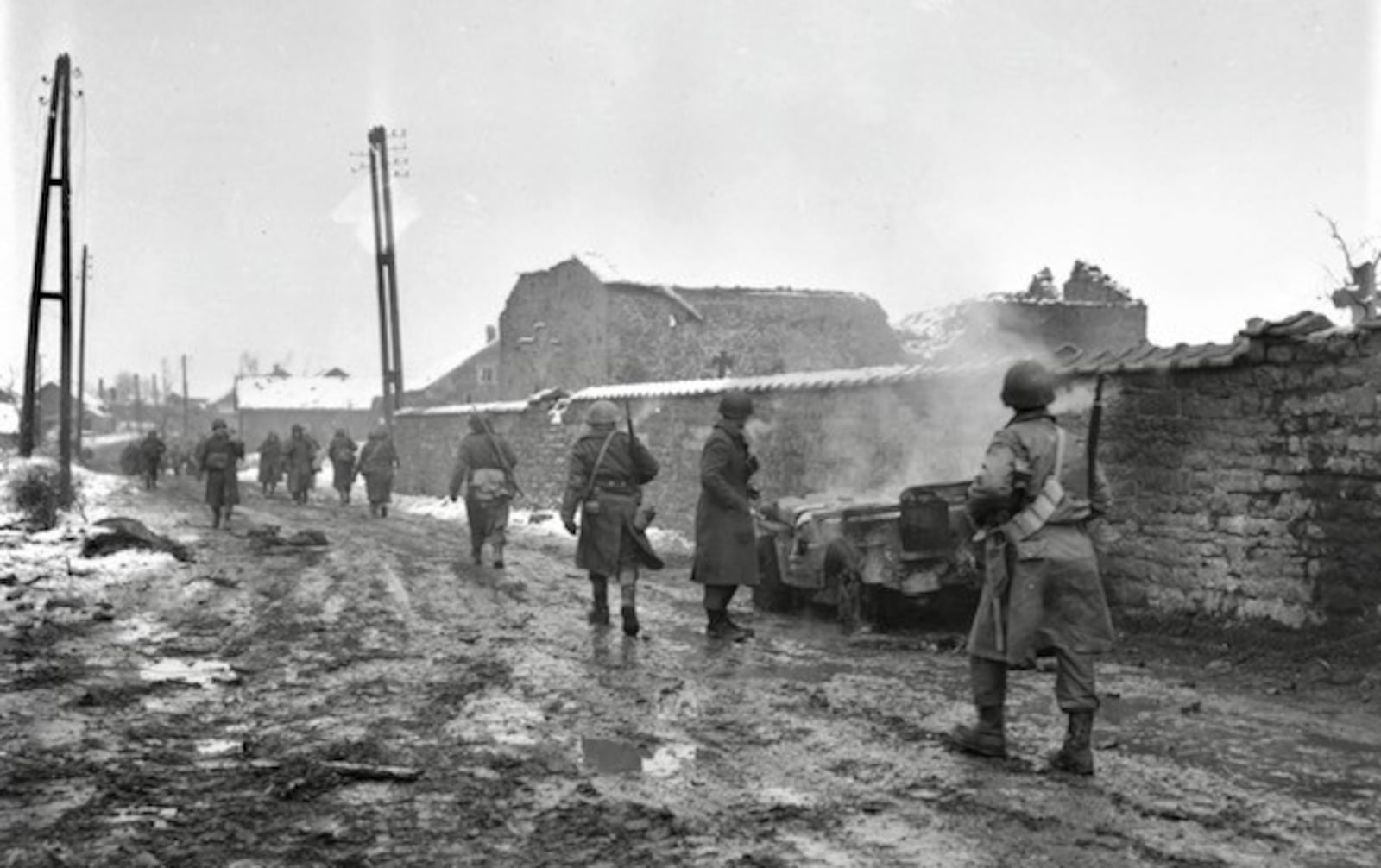 Infantrymen move along a road through Beffe, Belgium, which was hit by Nazi mortars.  The jeep at right was hit by shell.  Belgium.  1/5/45.  290th Regt. 75th Div.