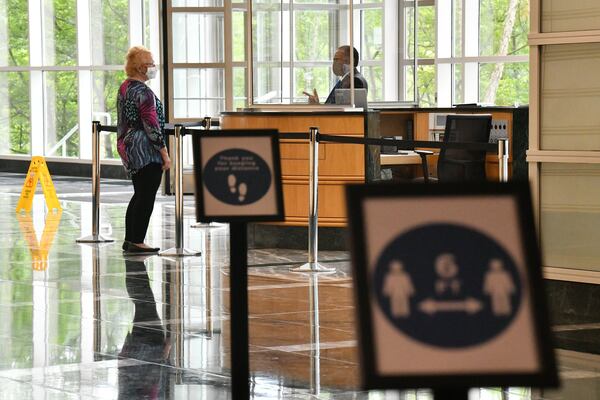 Clear plastic dividers were set up at the reception desk in the lobby of the One Overton Park building in Cobb County, where Gas South is headquartered. Shoppers are hitting stores and filling parking lots. Some diners are returning to sit-down restaurants. But many of metro Atlanta’s white-collar towers and office parks are still lonely places during the coronavirus pandemic. The restart of the economy is often doing so without a big return to cubicles, shared desks and many of the other trappings of corporate life. (Hyosub Shin / Hyosub.Shin@ajc.com)