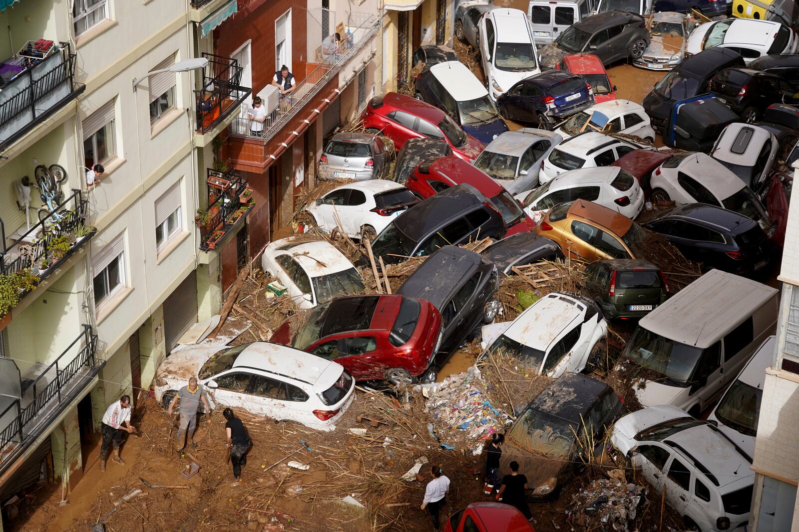 Residents clean the street next to cars piled up after being swept away by floods in Valencia, Spain, Wednesday, Oct. 30, 2024. (AP Photo/Alberto Saiz)