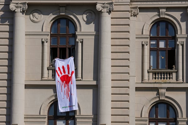 Opposition lawmakers hold a banner that shows a painted hand symbolizing blood, during a parliament session in Belgrade, Serbia, Tuesday, March 4, 2025. (AP Photo/Darko Vojinovic)