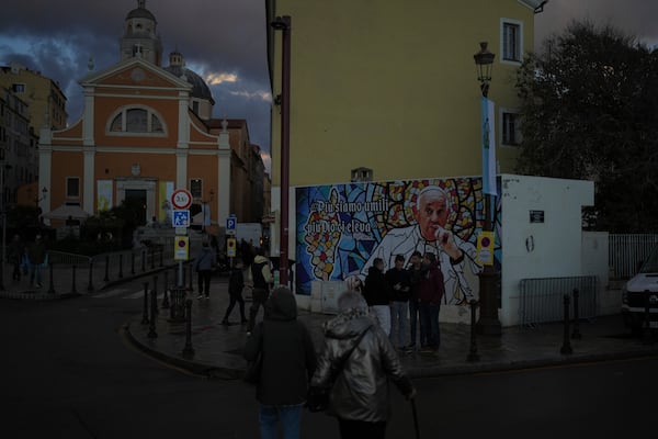 People walk past a mural featuring Pope Francis prior to the Pope's visit, in Ajaccio, in the southern French island of Corsica, Saturday, Dec. 14, 2024. (AP Photo/Thibault Camus)