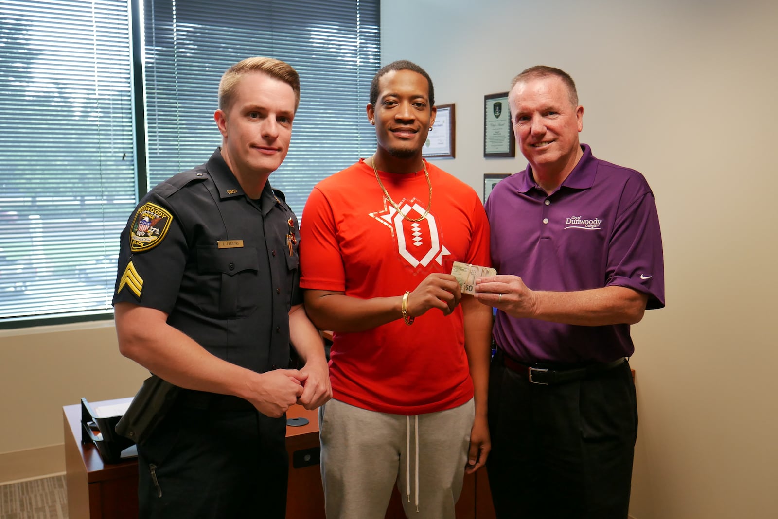 Randrell Lewis (center) poses with Dunwoody police Sgt. Robert Parsons (left) and Chief Billy Grogan after Lewis returned $2,100 he took from the “isolated cash storm” on I-285.