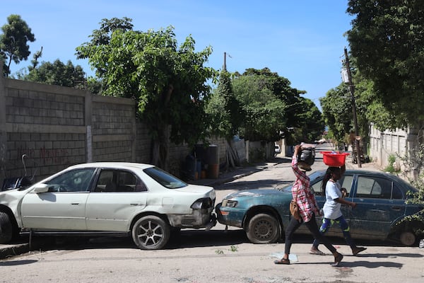 Pedestrians walk past vehicles serving as a barricade set up by residents to deter gang members from entering their neighborhood, in downtown Port-au-Prince, Haiti, Wednesday, Nov. 13, 2024. (AP Photo/Odelyn Joseph)