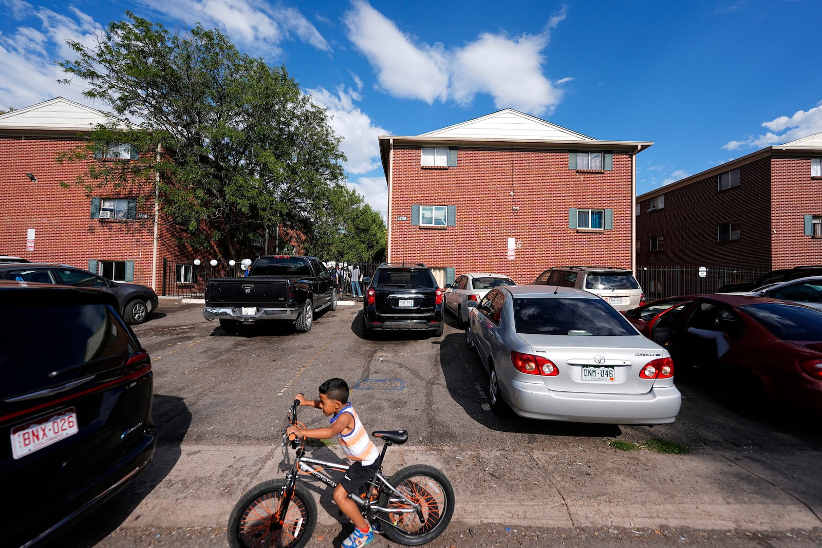 FILE - A boy guides his bicycle past apartment buildings as a rally organized by the East Colfax Community Collective is held in the courtyard to address chronic problems in the apartments occupied by people displaced from their home countries in central and South America, Tuesday, Sept. 3, 2024, in Aurora, Colo. (AP Photo/David Zalubowski, File)