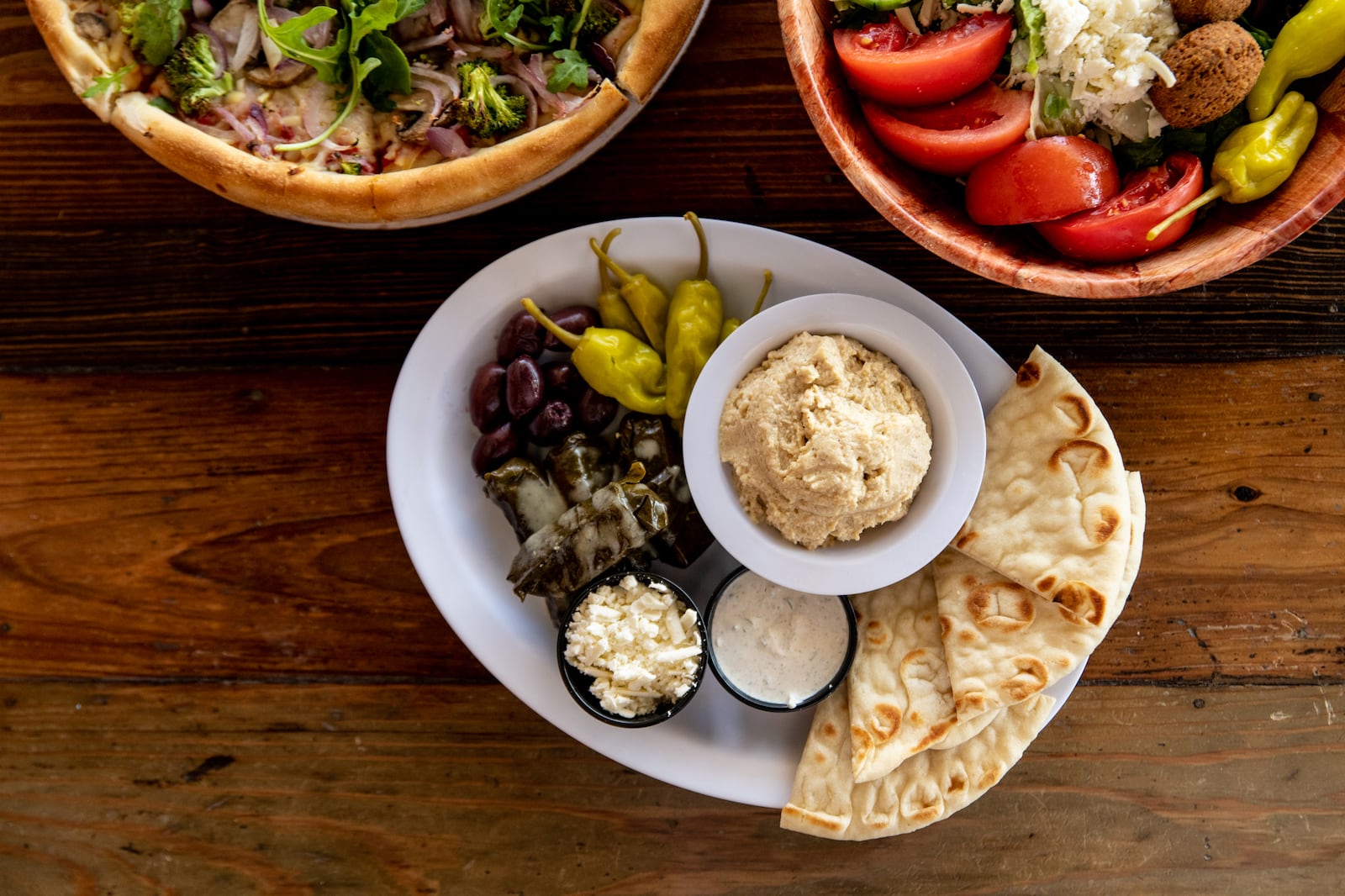 The Greek Pizzeria and Gyros Sampler Platter with dolmades, Kalamata olives, pepperoncini, tzatziki, hummus, and pita wedges. (Mia Yakel for The Atlanta Journal-Constitution)