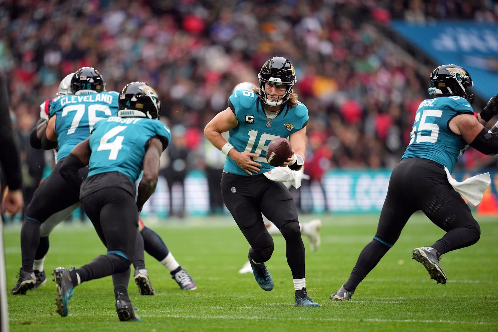 Jacksonville Jaguars quarterback Trevor Lawrence (16) hands off to running back Tank Bigsby (4) during the first half of an NFL football game against the New England Patriots, Sunday, Oct. 20, 2024, in London. (AP Photo/Kin Cheung)