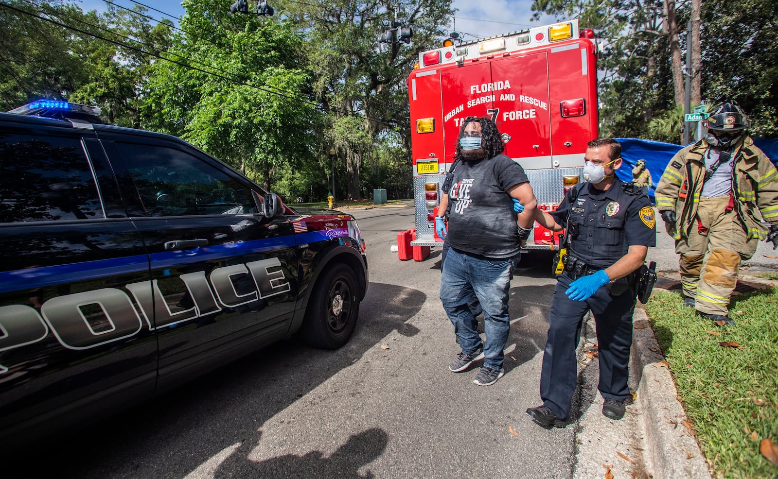 Protester Jordan Mazurek, 28, who cemented his hands in two 55-gallon plastic drums filled with concrete outside of the Governor's Mansion, is escorted by a Tallahassee Police Department officer in handcuffs to a vehicle, Friday, April 17, 2020. Mazurek is protesting how Gov. Ron DeSantis is handling coronavirus in state prisons. (Alicia Devine/Tallahassee Democrat via AP)